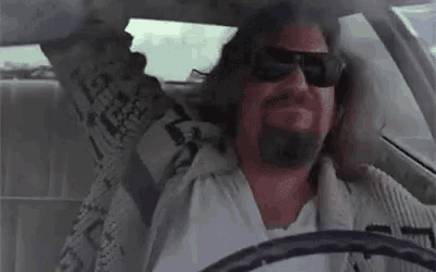 a man wearing sunglasses is driving a car with his arm in the air .