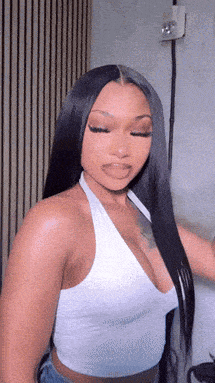 a woman with long black hair is wearing a white halter top and jeans .