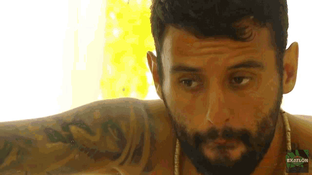 a man with a beard and a tattoo has the word exatlon on the bottom of his screen