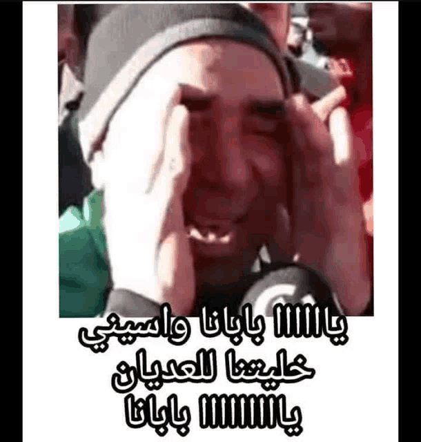 a man is crying with his hands on his face while wearing a hat .