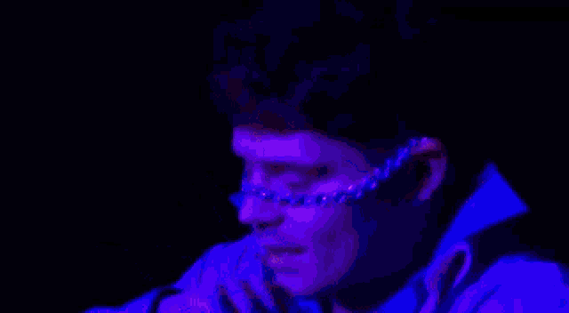 a close up of a person wearing glasses and a choker in a dark room with purple lights .