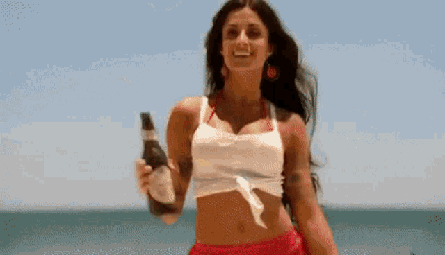 a woman in a red crop top is holding a can of beer .