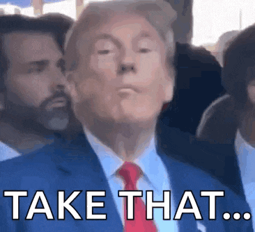donald trump is wearing a blue suit and red tie and making a funny face while standing in front of a crowd .