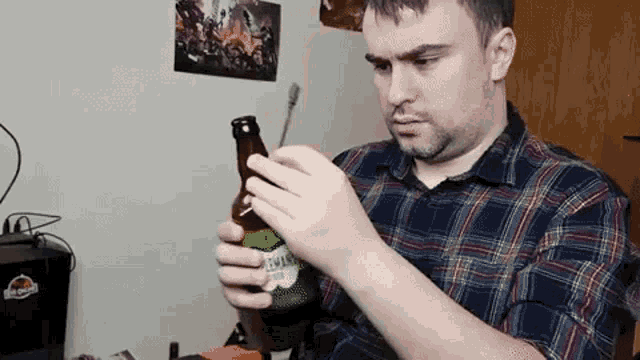 a man in a plaid shirt is holding a bottle of beer in his hand .