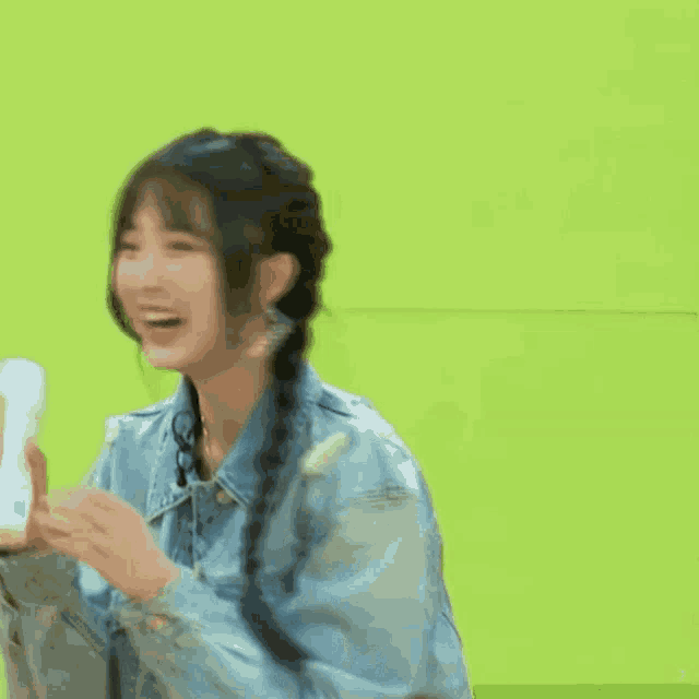 a woman in a denim jacket is standing in front of a green screen .
