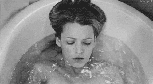 a black and white photo of a woman laying in a bathtub .