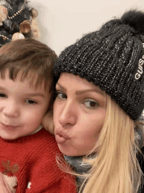 a woman wearing a black guess hat holds a little boy