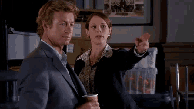 a man in a suit stands next to a woman in a black jacket with a cup of coffee in her hand