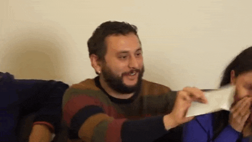 a man with a beard is holding a piece of paper in his hands while sitting next to a woman .
