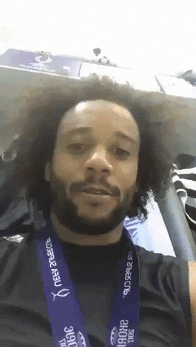 a man with curly hair and a beard wears a purple lanyard that says new zealand on it