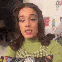 a woman wearing a green sweater and overalls is making a face