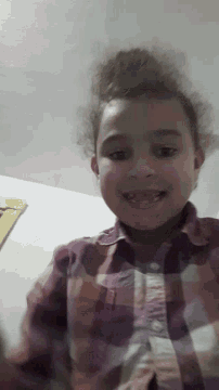 a little girl wearing a purple plaid shirt is smiling