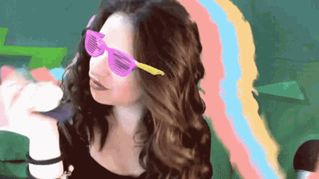 a woman wearing sunglasses holds a microphone in front of a colorful background