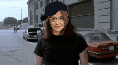 a woman wearing glasses and a baseball cap is standing in front of a red car