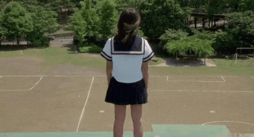 a girl in a school uniform is standing on a ledge overlooking a soccer field