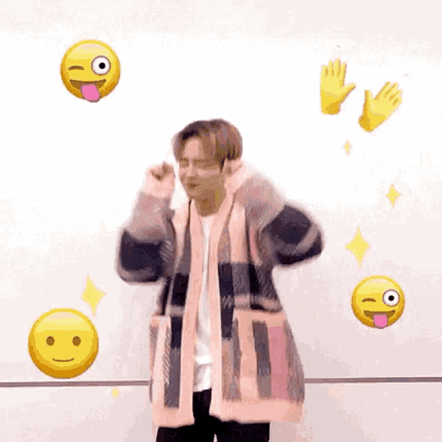 a man in a plaid sweater is standing in front of a white wall with emojis .