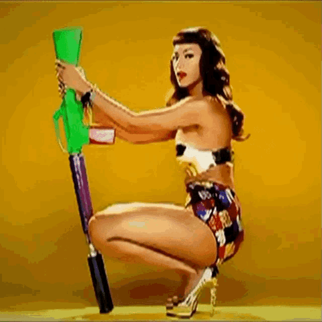 a woman in a bikini is squatting down while holding a water gun .