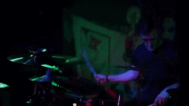 a man playing drums in a dark room with a sign that says t.v. on it