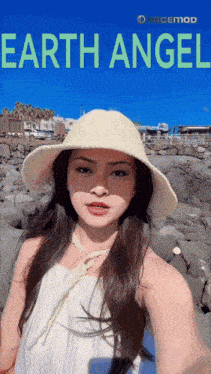 a woman wearing a hat takes a selfie in front of an earth angel poster