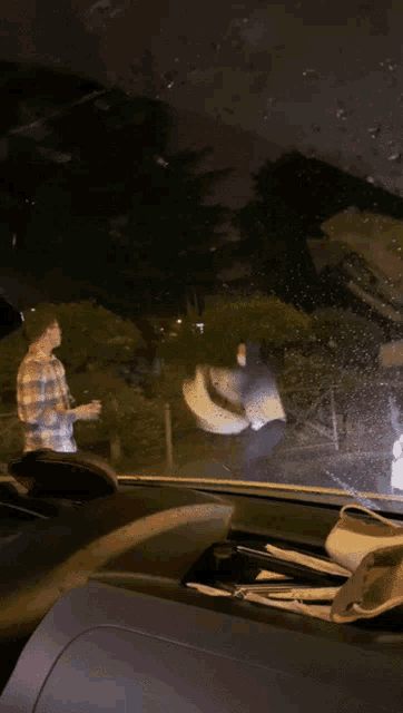 a car windshield is covered in rain drops and a person is standing in the background