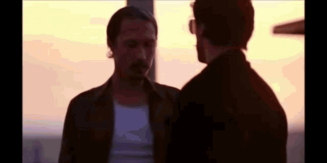 two men are standing next to each other in front of a sunset and talking to each other .