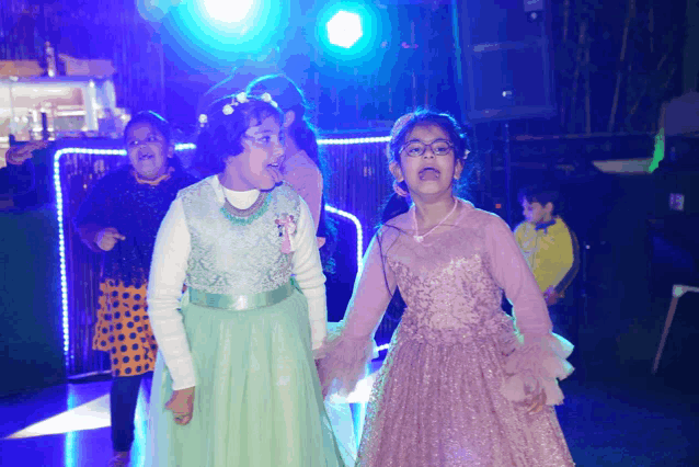 a girl in a pink dress and a girl in a green dress are on a dance floor