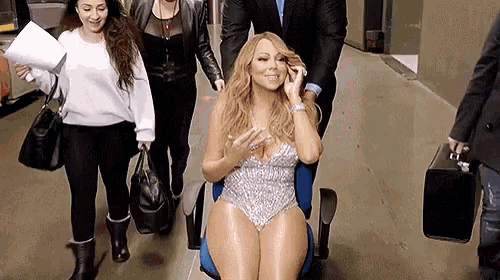 a woman in a swimsuit is sitting in a chair talking on a cell phone while people walk behind her .