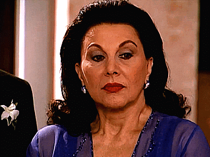 a woman in a blue dress with a flower in her hair looks at the camera
