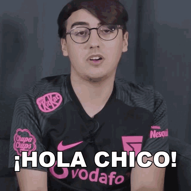a man wearing glasses and a kitkat shirt says hola chico in spanish