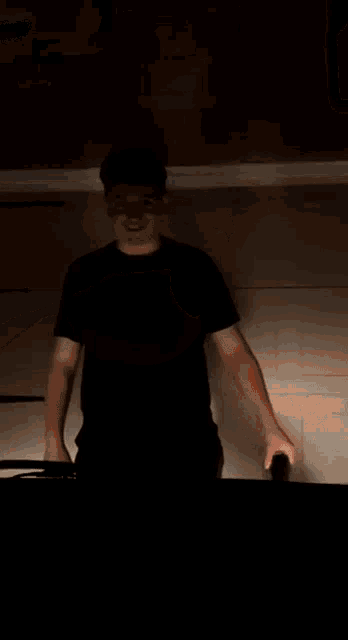 a man in a black t-shirt is standing in a dark room .
