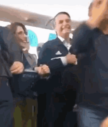 a group of people are dancing on a plane and one man is wearing an adidas jacket