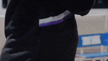 a person wearing a black jacket has a purple zipper on the back pocket