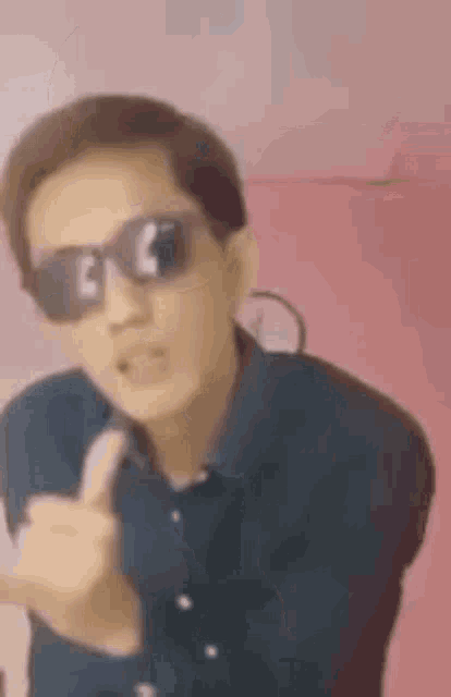 a man wearing sunglasses and a blue shirt is giving the middle finger .