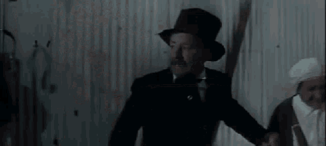 a man in a tuxedo is standing in a dark room surrounded by a bunch of white flags .