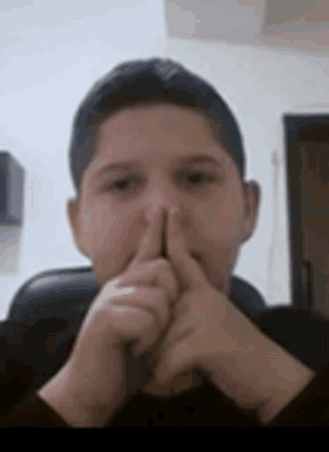a young boy is sitting in a chair with his hands on his face and giving a thumbs up .