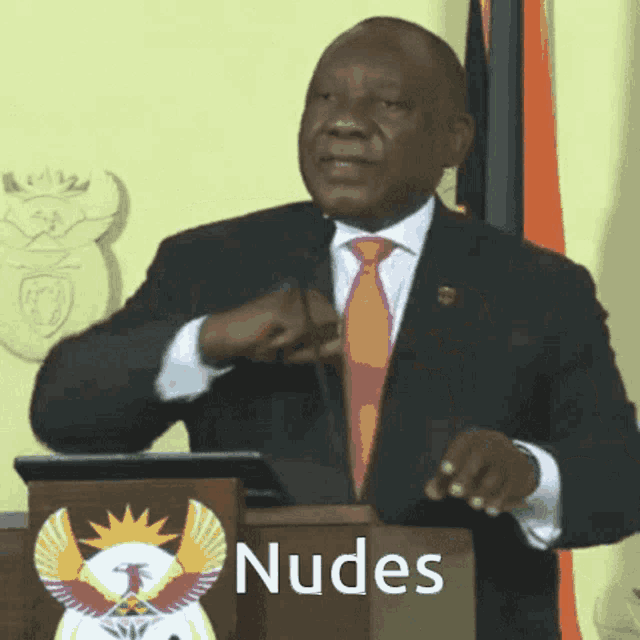 a man in a suit and tie stands behind a podium with the words nudes written on it