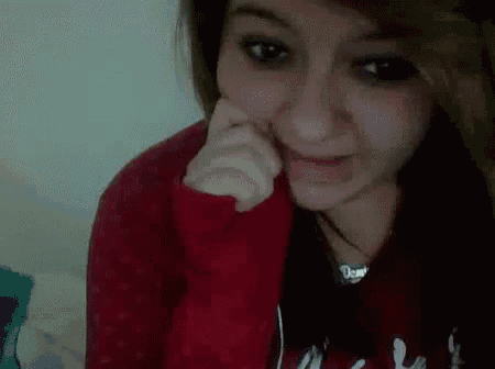 a girl in a red sweater is making a funny face with her hand on her face .