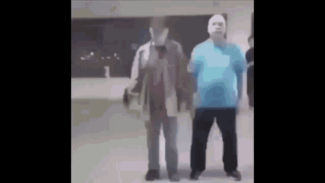 two men are standing next to each other in a room . one of the men is wearing a mask .
