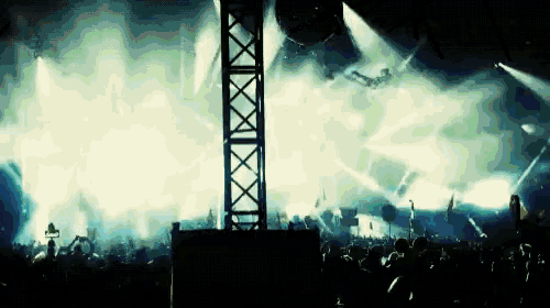 a crowd of people watching a concert with a tower in the background