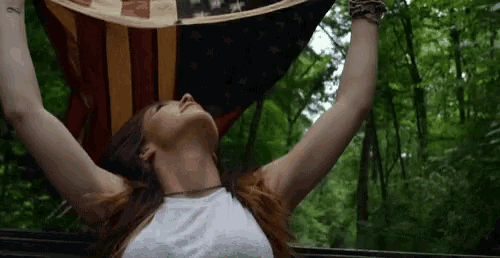a woman with her arms outstretched holds an american flag over her head