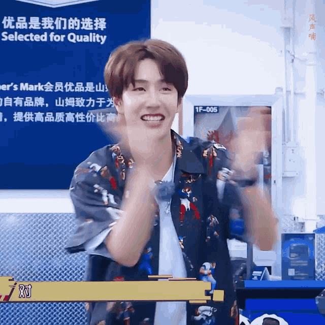 a man wearing a hawaiian shirt is clapping in front of a sign that says " selected for quality "