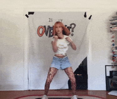 a woman is dancing in front of a sign that says is it over ?