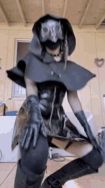 a woman in a black costume with a skull mask on her face is standing in a room .