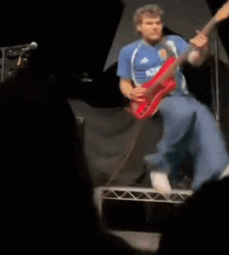 a man in a blue shirt is playing a red electric guitar on stage