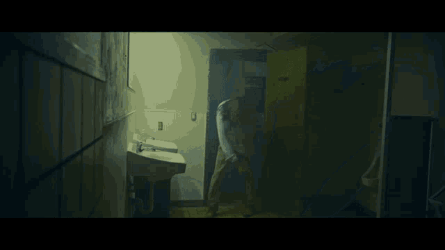 a man in a blue shirt is standing in a dark bathroom next to a sink