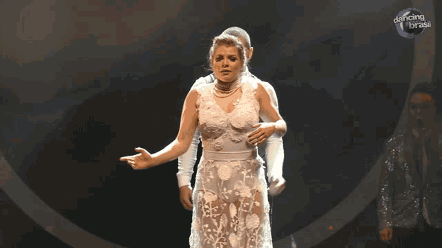a woman in a white dress is being held by a man on a stage with dancing brasil written in the background