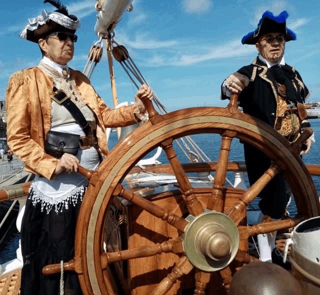a man and a woman dressed in pirate costumes are behind a wooden ship steering wheel