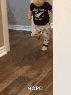 a baby is running across a wooden floor while wearing a black shirt .