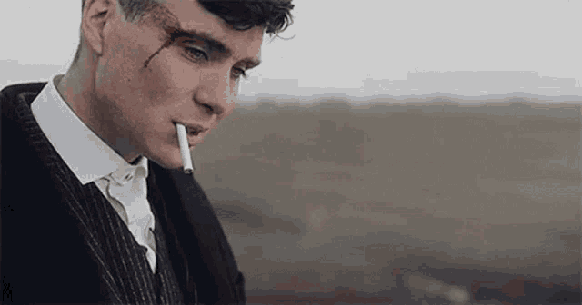 a man in a suit is smoking a cigarette in a field .