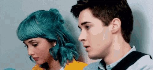a man and a woman with blue hair are looking at each other .